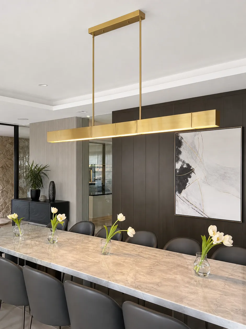 Linear chandelier lighting fixture in brushed gold finish suspended over a long commercial dining table