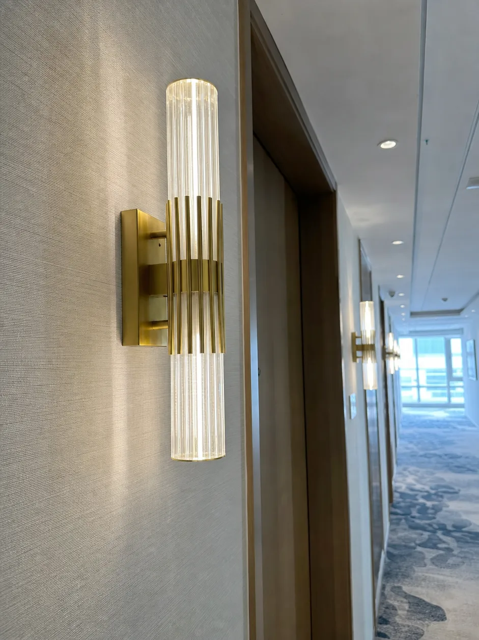 Custom wall sconce with die-cast aluminum housing and brushed gold finish, installed in a hospitality corridor