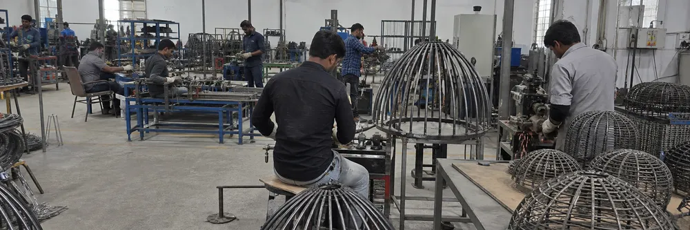 Industrial pendant lighting production — steel cage frames being formed and welded on dedicated bending fixtures in the factory