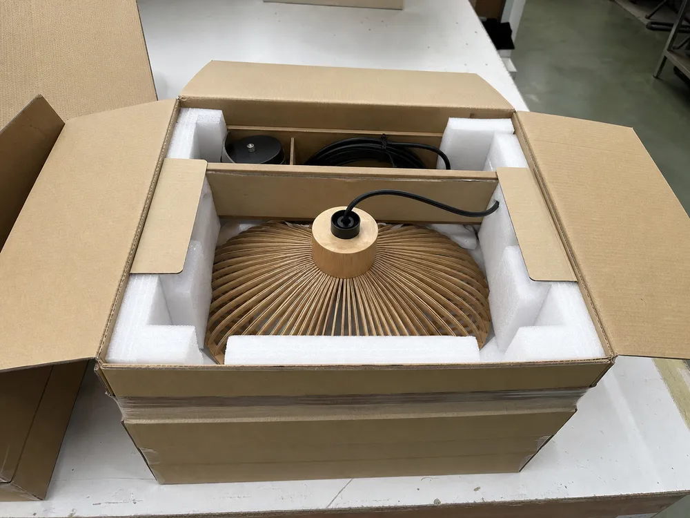 Export packaging for wood pendant lighting showing foam-lined carton with corner protection and cable management