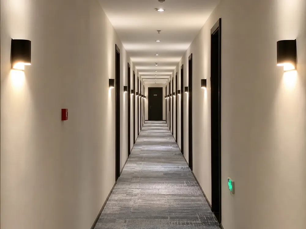 Hotel corridor with uniform wall sconce lighting along both sides, demonstrating batch consistency in a hospitality installation