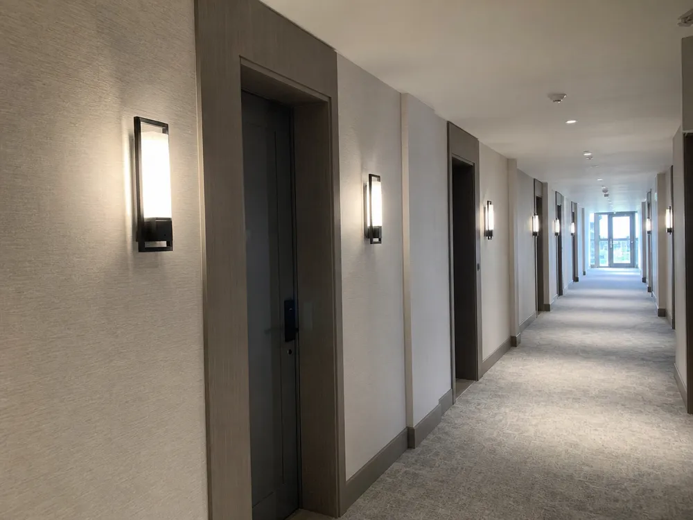 High-rise residential corridor with consistent wall lighting fixtures at unit entrances