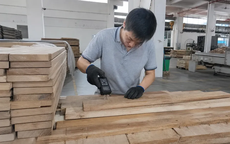 Pin-type moisture meter testing kiln-dried hardwood plank during incoming material inspection