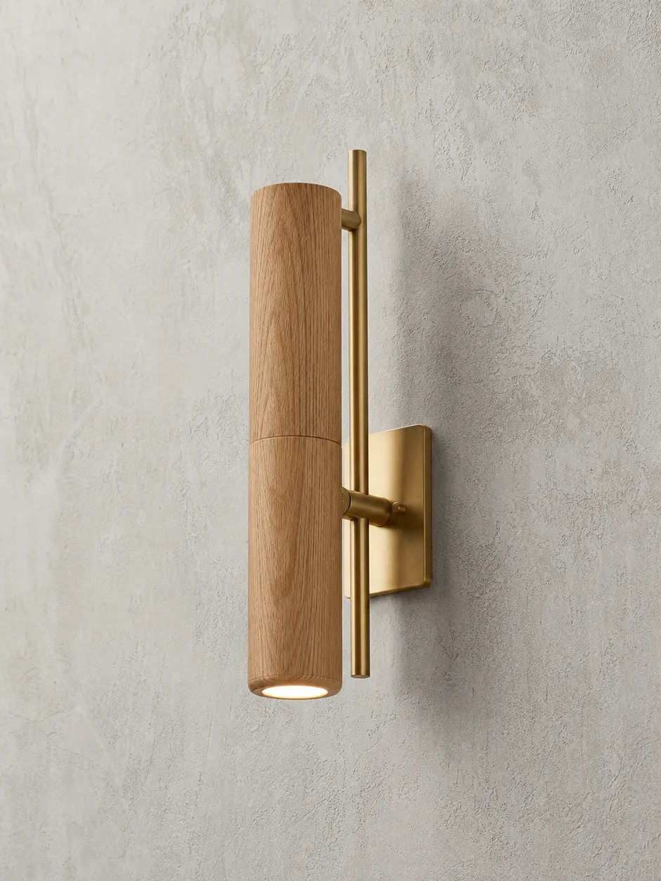 Wooden wall lighting sconce featuring kiln-dried oak body with brushed gold metal hardware, mounted on a textured wall